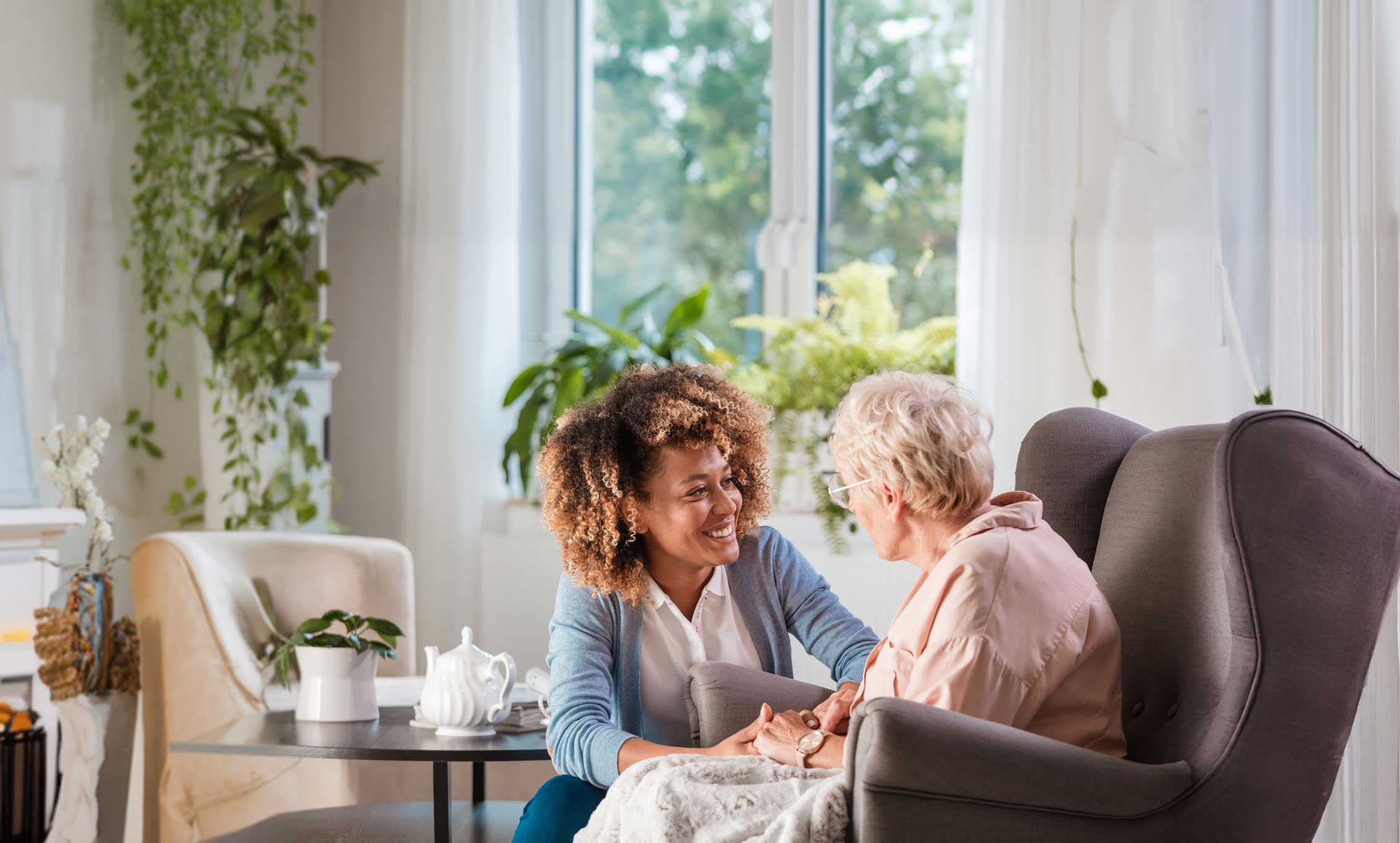 Betreuungskraft und Seniorin sitzen gemeinsam am Tisch